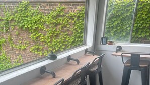 A wooden table with four chairs, a window with a view of a brick wall and greenery, and a small shelf with a teapot and a bowl. - Historic Haven Hideaway California King Bed

 (Cleveland)