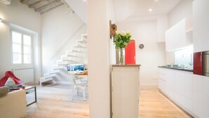 A modern interior with a staircase leading to a dining area, a kitchen with white cabinets, and a living space with a sofa and a coffee table. - Apartments Florence - Casa Amici (Firenze)