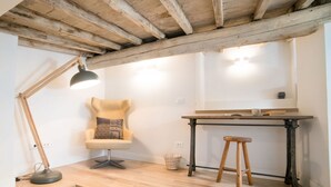 A room with a wooden ceiling, a chair with a cushion, a desk, a stool, and a lamp. - Apartments Florence - Casa Amici (Firenze)