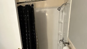 Una ducha con puerta de vidrio, barra para toallas y cortina de baño.