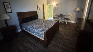 Un dormitorio con cama, mesita de noche, lámpara, silla y una pequeña mesa con otra silla.