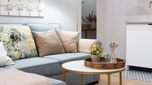 Ein Wohnzimmer mit einem hellblauen Sofa, beigen Kissen, einem runden Couchtisch mit einem gewebten Korb und einer Stehlampe.
