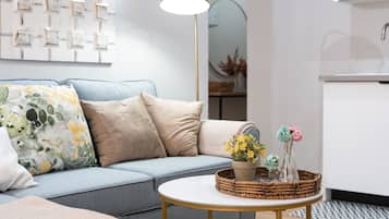 A living room with a light blue sofa, beige cushions, a round coffee table with a woven basket, and a floor lamp.