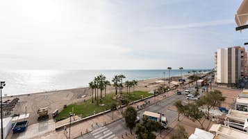 A coastal street with a beach, palm trees, and a pedestrian crossing.