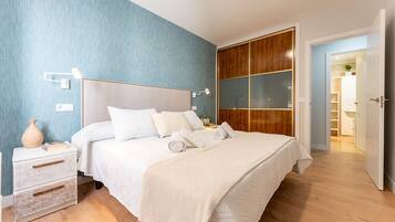 A bedroom with a bed, bedside tables, a nightstand, a wooden wardrobe, and a door leading to another room.