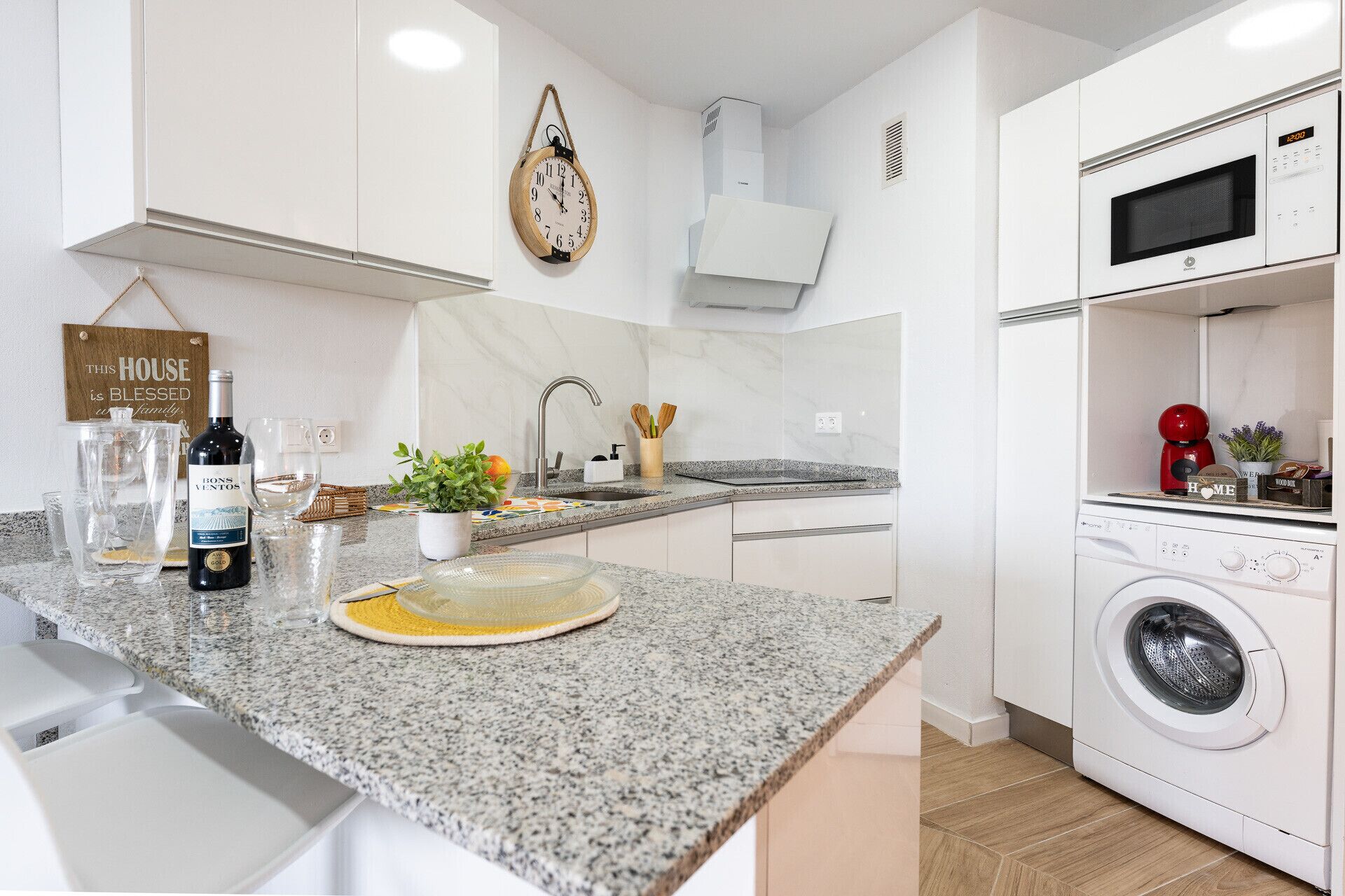 A modern kitchen with granite countertops, a built-in oven, microwave, and a washing machine.