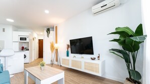A modern living room with a wooden floor, a white sofa, a coffee table, a TV, and a large plant. - MalagaSuite Cozy Studio & Pool Torremolinos (Torremolinos)