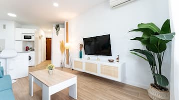Una sala de estar moderna con piso de madera, un sofá blanco, una mesa de centro, un televisor y una planta grande.