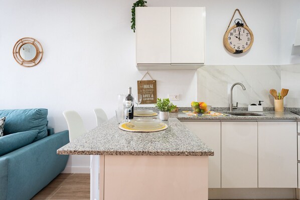 A modern kitchen with white cabinets, a granite countertop, and a hanging wooden clock. - MalagaSuite Cozy Studio & Pool Torremolinos (Torremolinos)