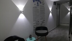 A hallway with two black chairs, a small table with a decorative item, and a wall with text and light fixtures. - Almaviva Casa Hotel (Medellín)