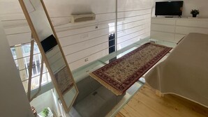 A high-ceilinged room with a large mirror, a flat-screen TV, and a wooden floor.