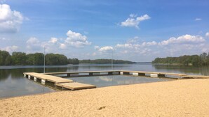 Une plage de sable avec des quais en bois qui s’étendent dans un lac paisible, le tout entouré d’arbres.