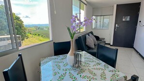 Un coin repas avec une table recouverte d’une nappe à motifs floraux, des chaises et un vase rempli de fleurs violettes.