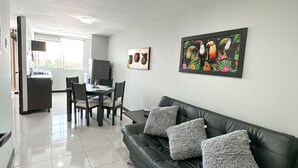 Un salon moderne avec un canapé en cuir noir, un coin repas avec une table et des chaises, et une cuisine équipée d’un réfrigérateur et d’une cuisinière.