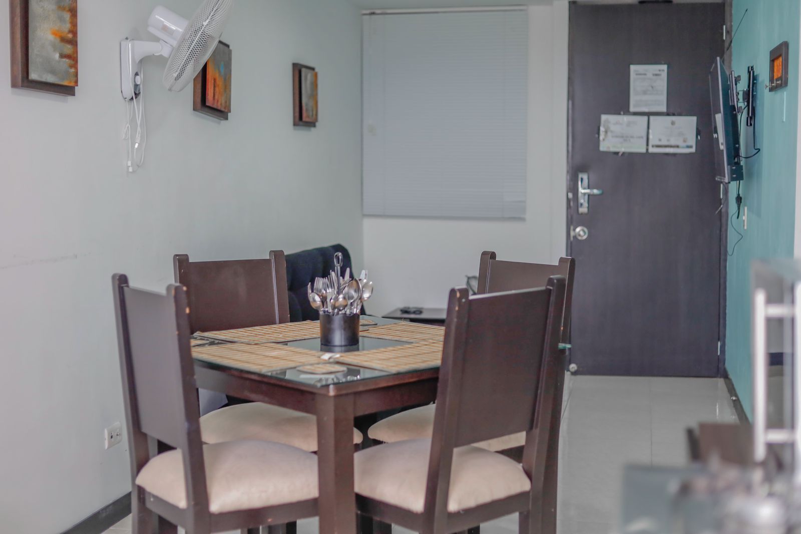 Un coin repas comprenant une table ronde, quatre chaises, un ventilateur et une petite table sur laquelle sont posés des ustensiles.