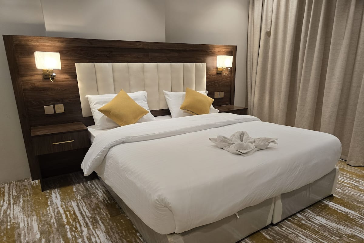 A neatly made bed with white linens, two pillows, and a towel arranged on the bed. There is a wooden headboard with two wall-mounted lights.