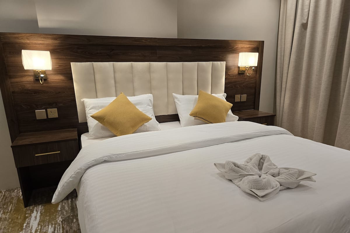 A hotel room with a large bed, two nightstands, a headboard with wall sconces, and a towel on the bed.