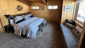Un dormitorio acogedor en una cabaña de madera, con una cama grande, un banco y dos ventanas pequeñas.
