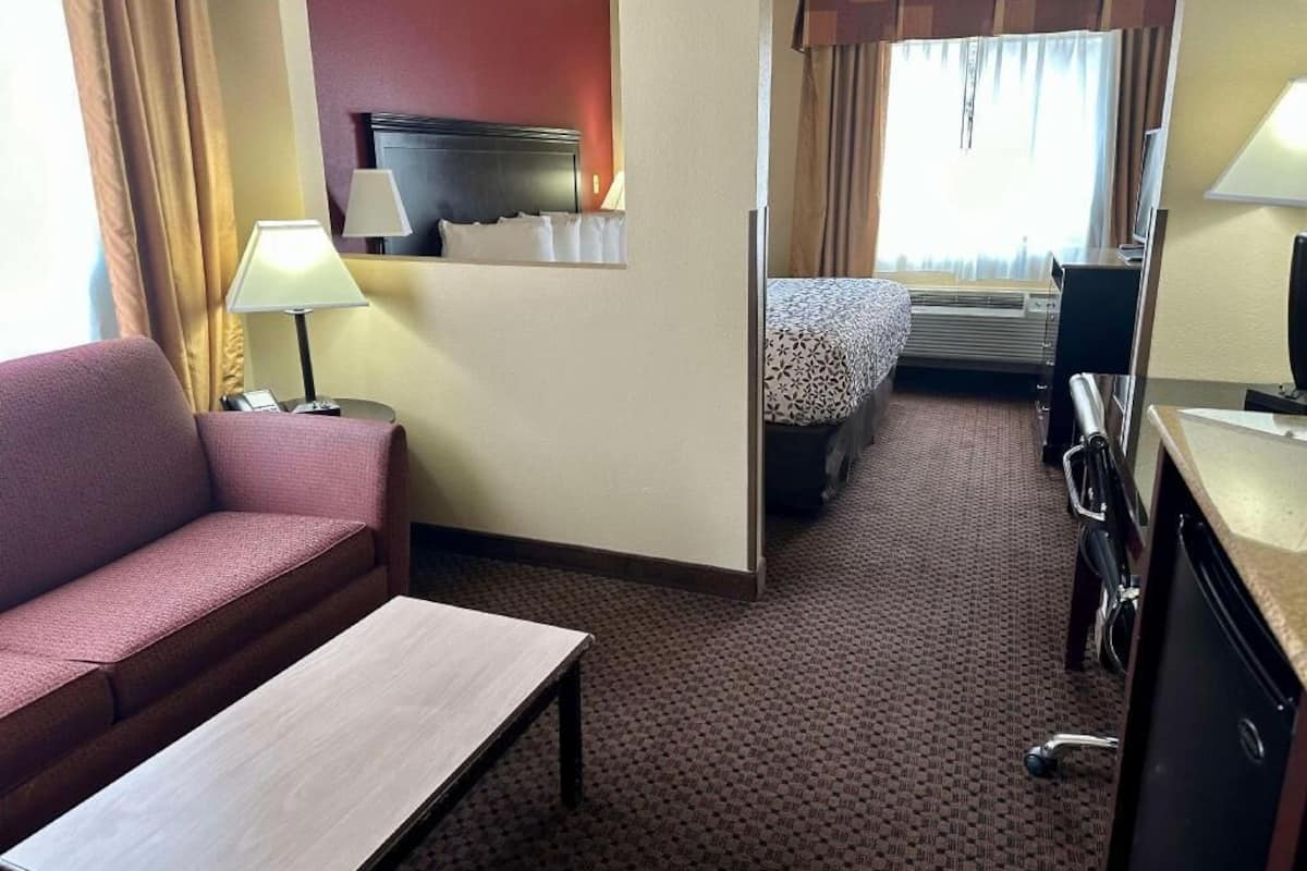 A hotel room with a sofa, a small table, a bed with a patterned bedspread, a desk with a chair, and a television.
