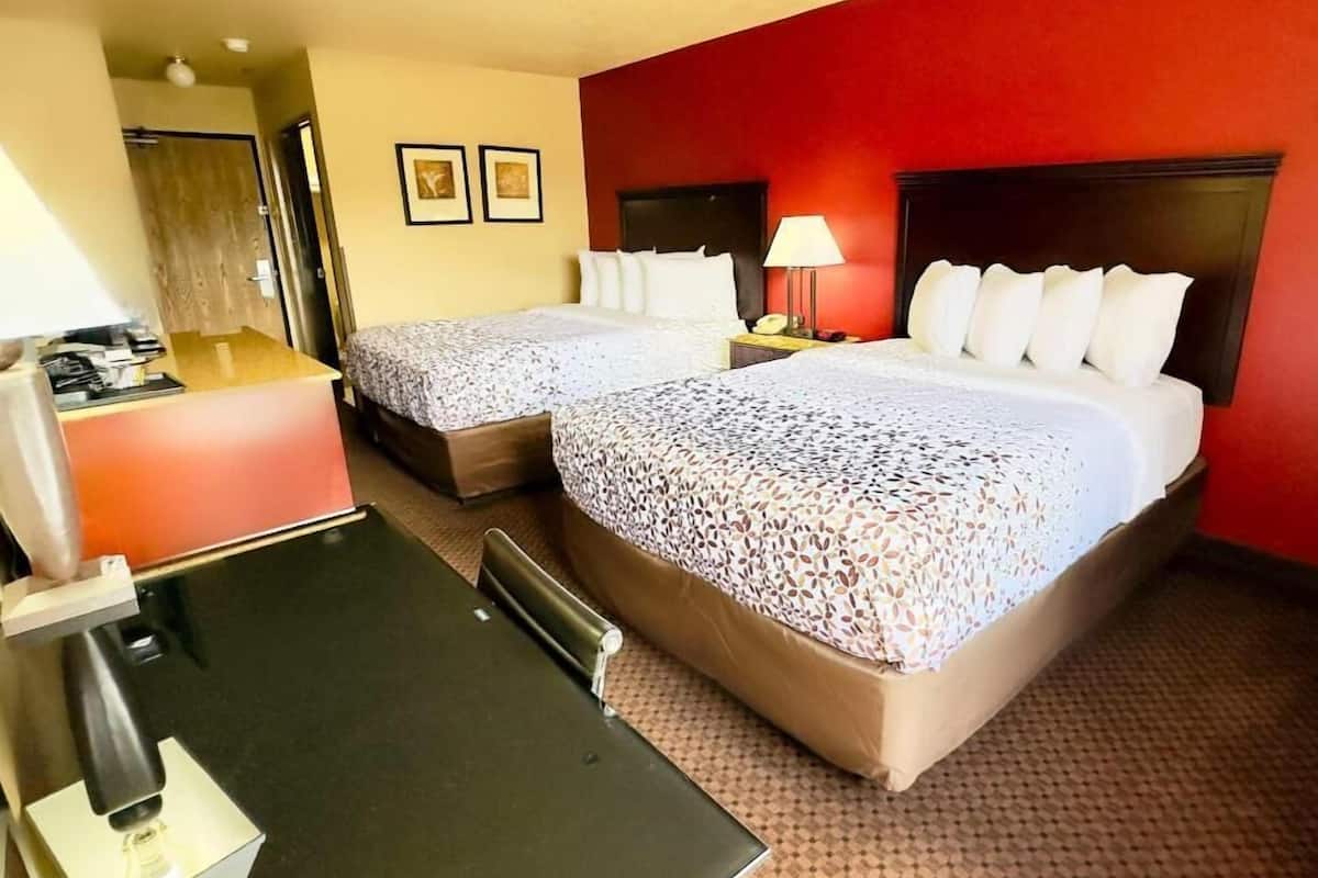 A hotel room with two beds, a desk, a chair, a lamp, and a telephone.