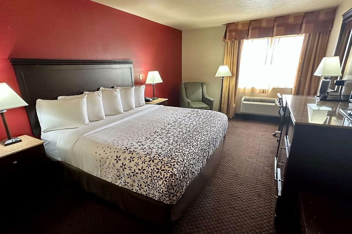 A hotel room with a large bed, two bedside lamps, a chair, a desk with a computer, and a window with curtains.