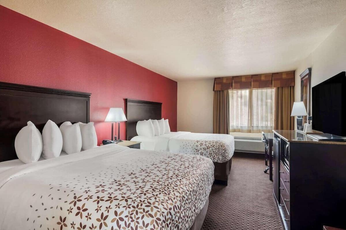 A hotel room with two beds, a desk, a TV, and a window with curtains.