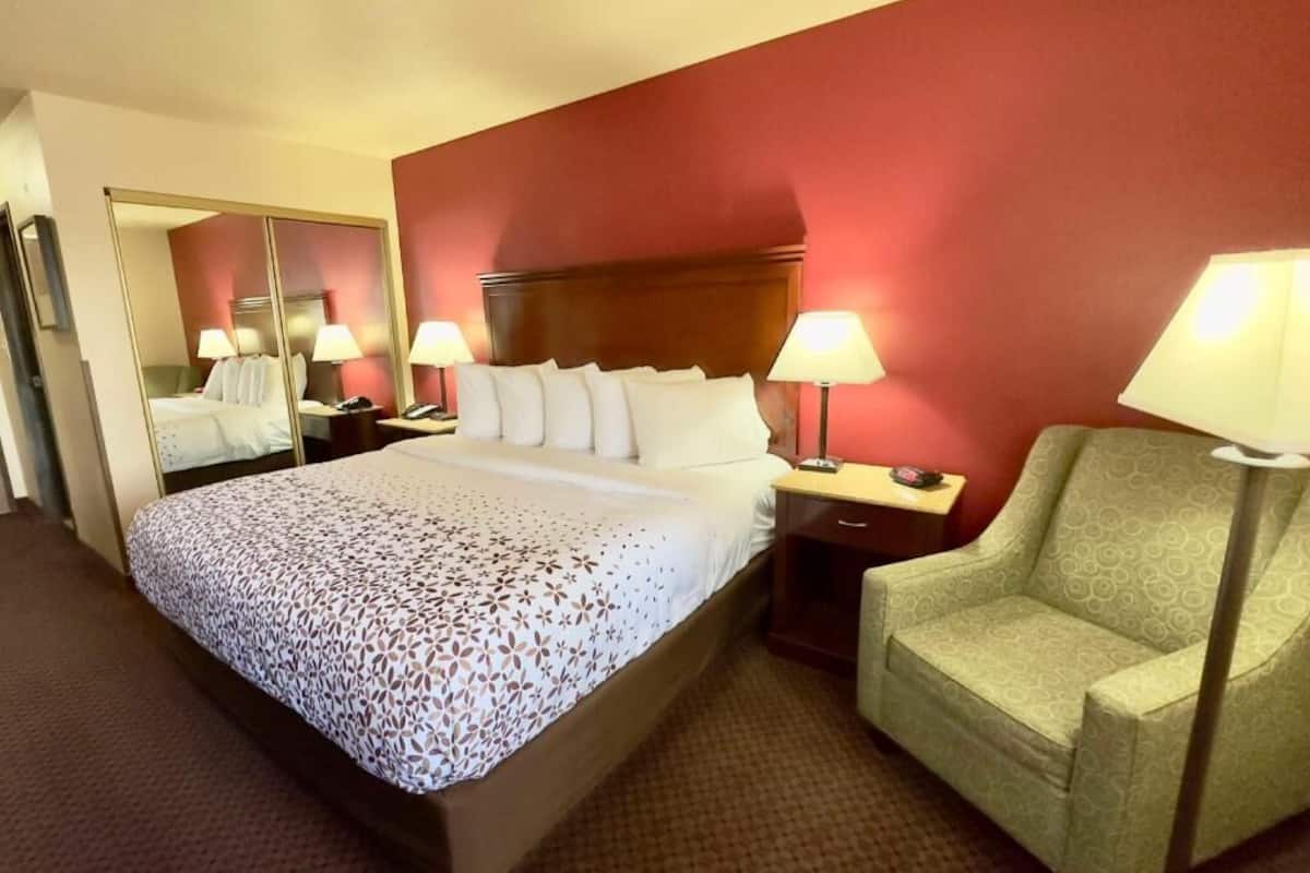 A hotel room with a large bed, two bedside lamps, a chair, and a mirror.