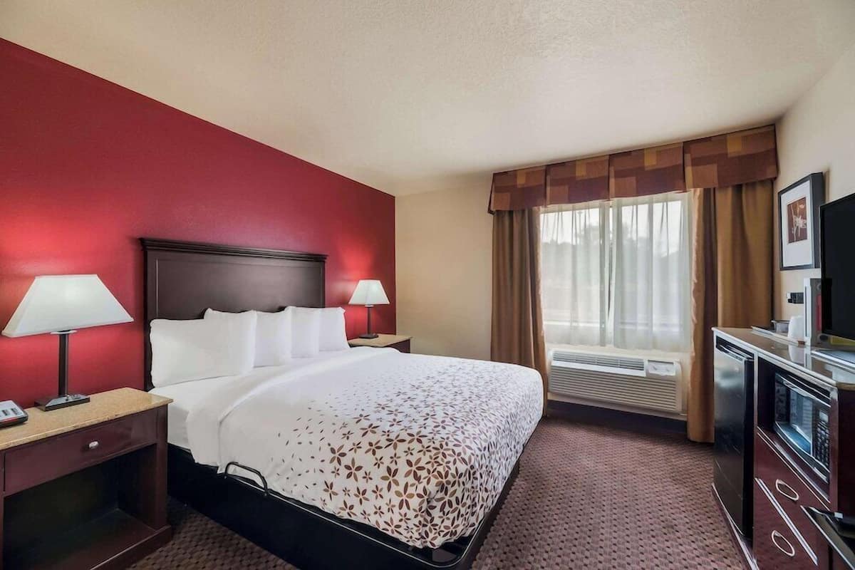 A hotel room with a bed, bedside lamps, a television, a desk with a phone, and a window with curtains.