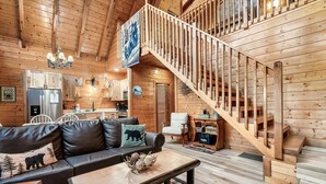 Un interior de cabaña acogedor con una escalera de madera, un sofá de cuero, un comedor y una cocina.