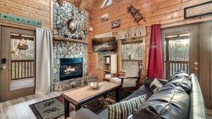 Interior acogedor de una cabaña con chimenea de piedra, sofá de cuero y techo de madera.
