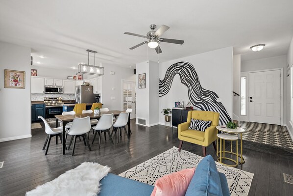 A modern living room with a dining area, a yellow armchair, and a large black and white mural on the wall.