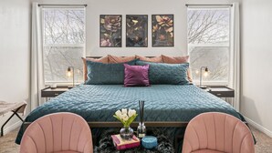 Une chambre à coucher avec un grand lit, deux tables de chevet, une commode, une chaise et une fenêtre avec des stores.