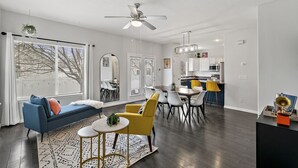 Un salon moderne avec un canapé bleu, des fauteuils jaunes et un coin repas comprenant une table et des chaises blanches.