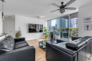 A modern living room with a black leather sofa, a glass coffee table, and a ceiling fan.