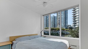 Ein Schlafzimmer mit großem Fenster, einem Bett, einem Nachttisch und einem Deckenventilator.