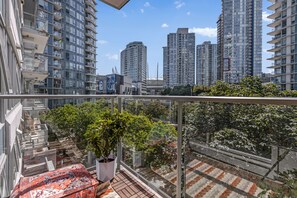 A balcony with a potted plant, a patterned rug, and a view of high-rise buildings.
