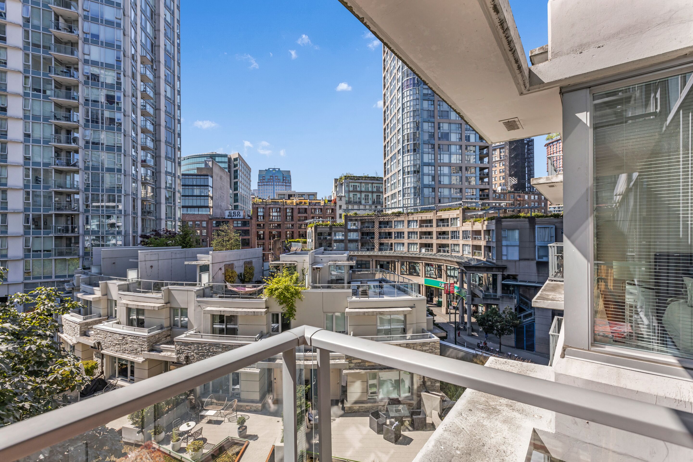 A high-rise residential building with multiple balconies, a rooftop garden, and a view of other high-rise buildings.