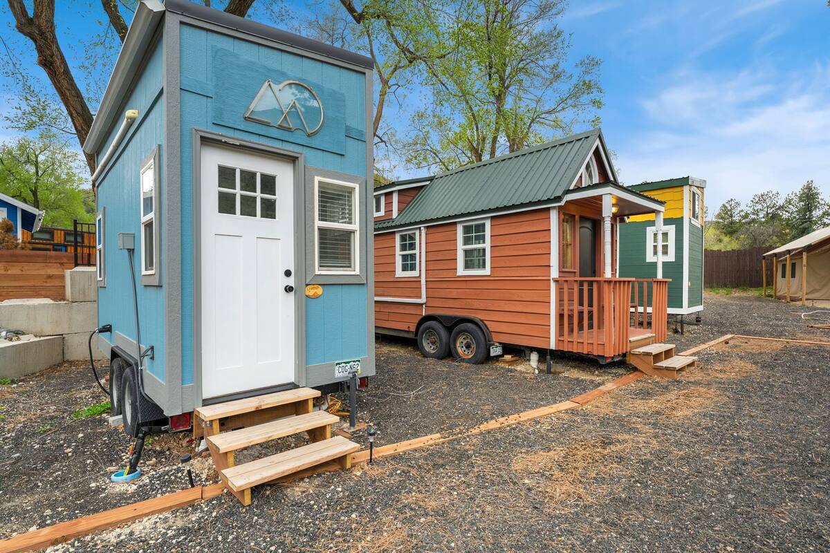 A small, blue mobile home with a white door and windows, a porch, and a ramp leading to the door.