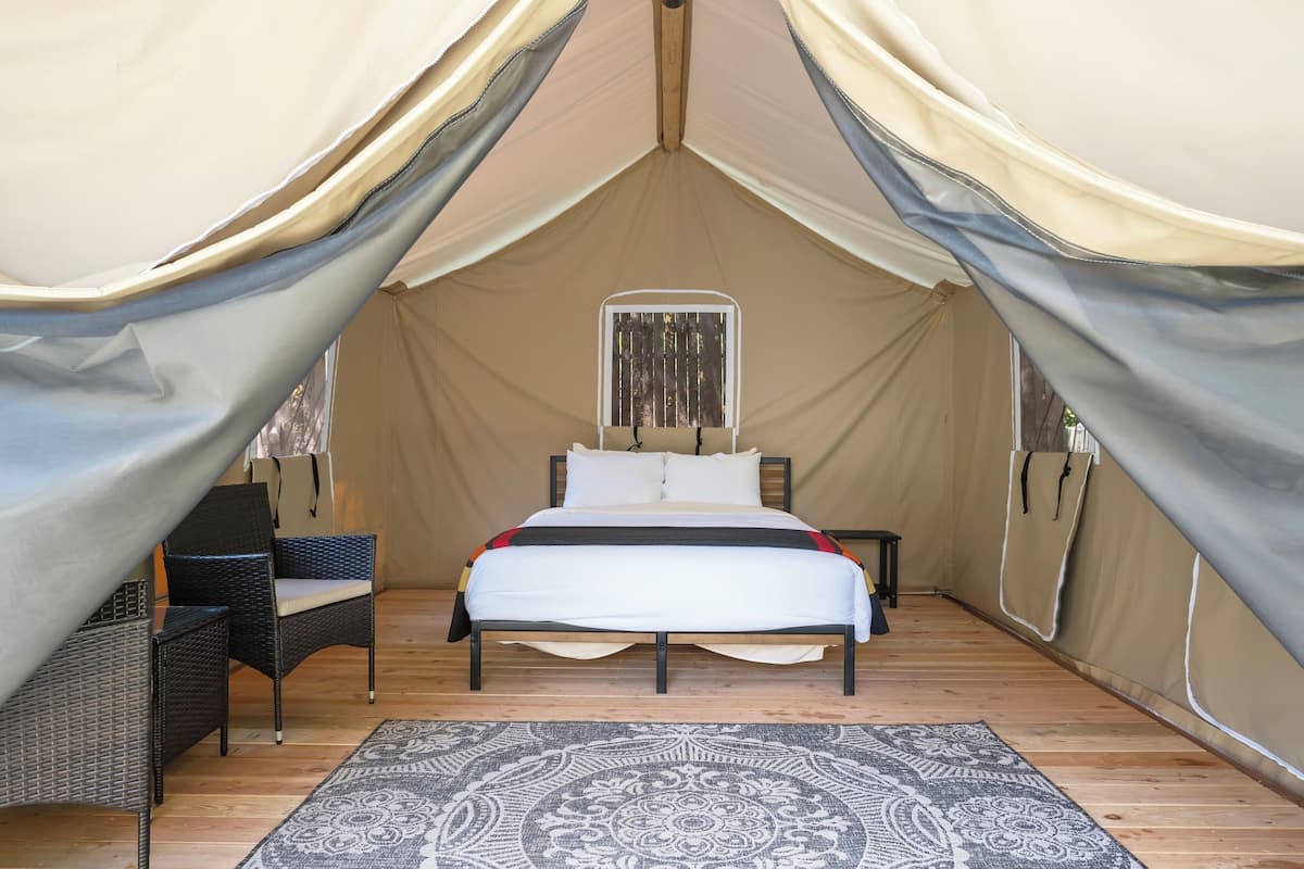 A tented accommodation with a bed, two chairs, and a patterned rug.