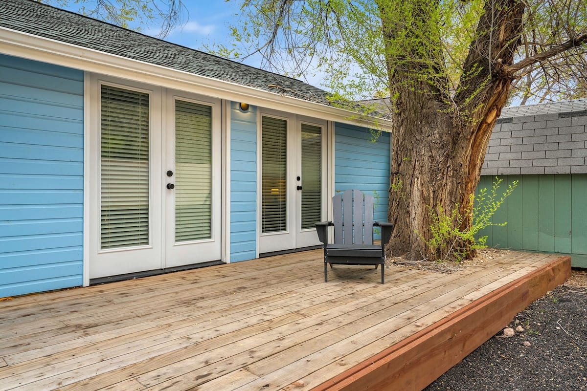 A blue house with a wooden deck, a chair, and a tree.