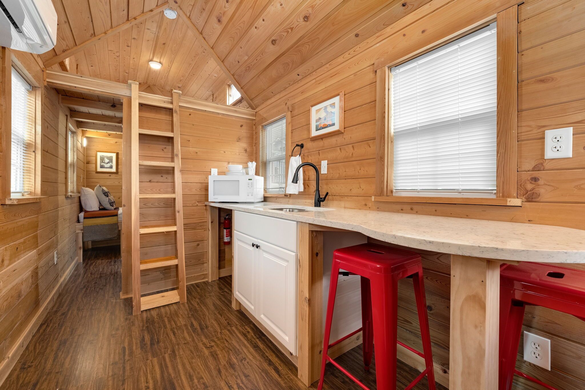 A compact wooden cabin with a kitchenette, a small seating area, and a ladder leading to a loft.