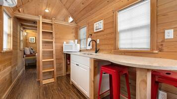 A compact wooden cabin with a kitchenette, a small seating area, and a ladder leading to a loft.