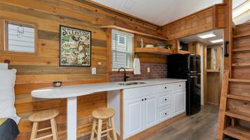 A compact kitchen with wooden walls, a white countertop, and a black refrigerator.
