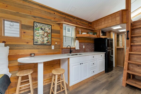 Una cocina compacta con paredes de madera, una encimera blanca y un refrigerador negro.