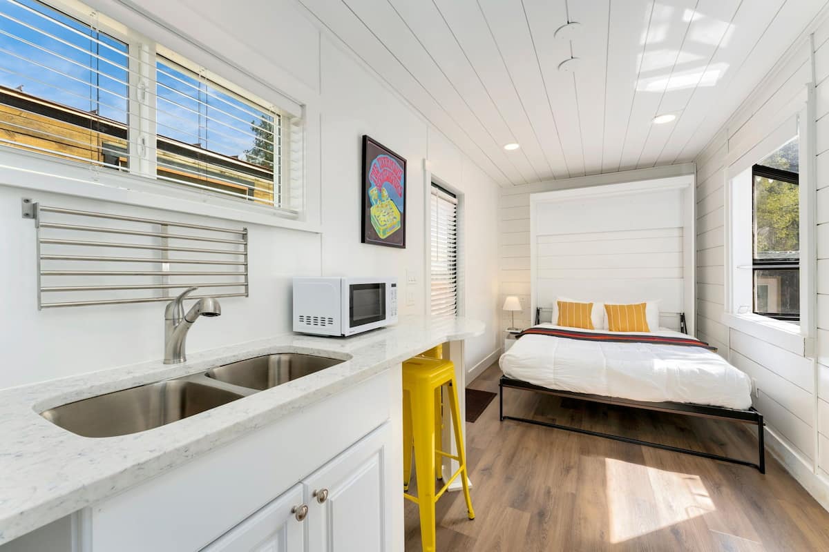 A compact bedroom with a bed, a window, and a kitchenette with a microwave.