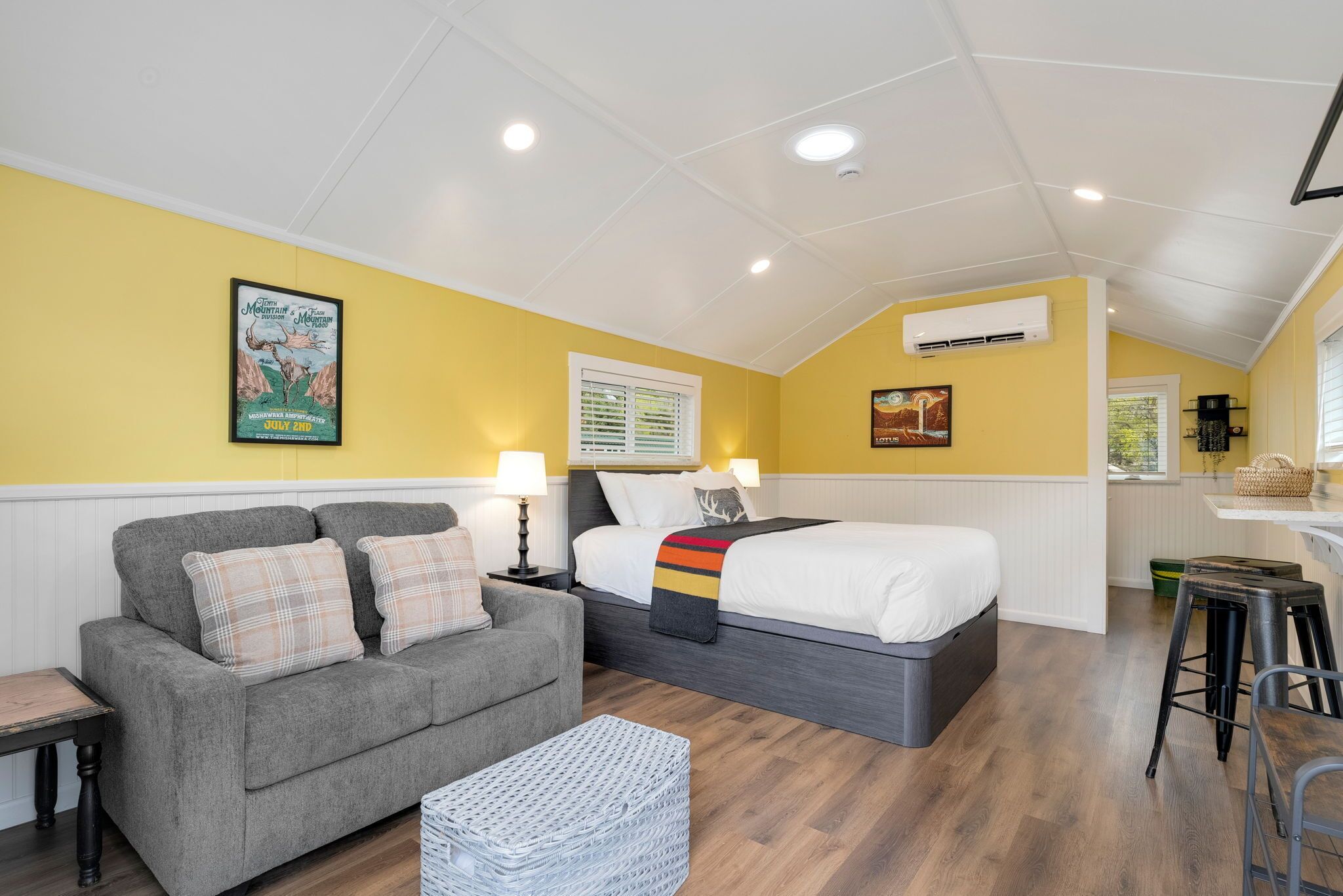 Quarto com sofá, cama, mesa pequena, luminária e ar-condicionado fixado na parede.