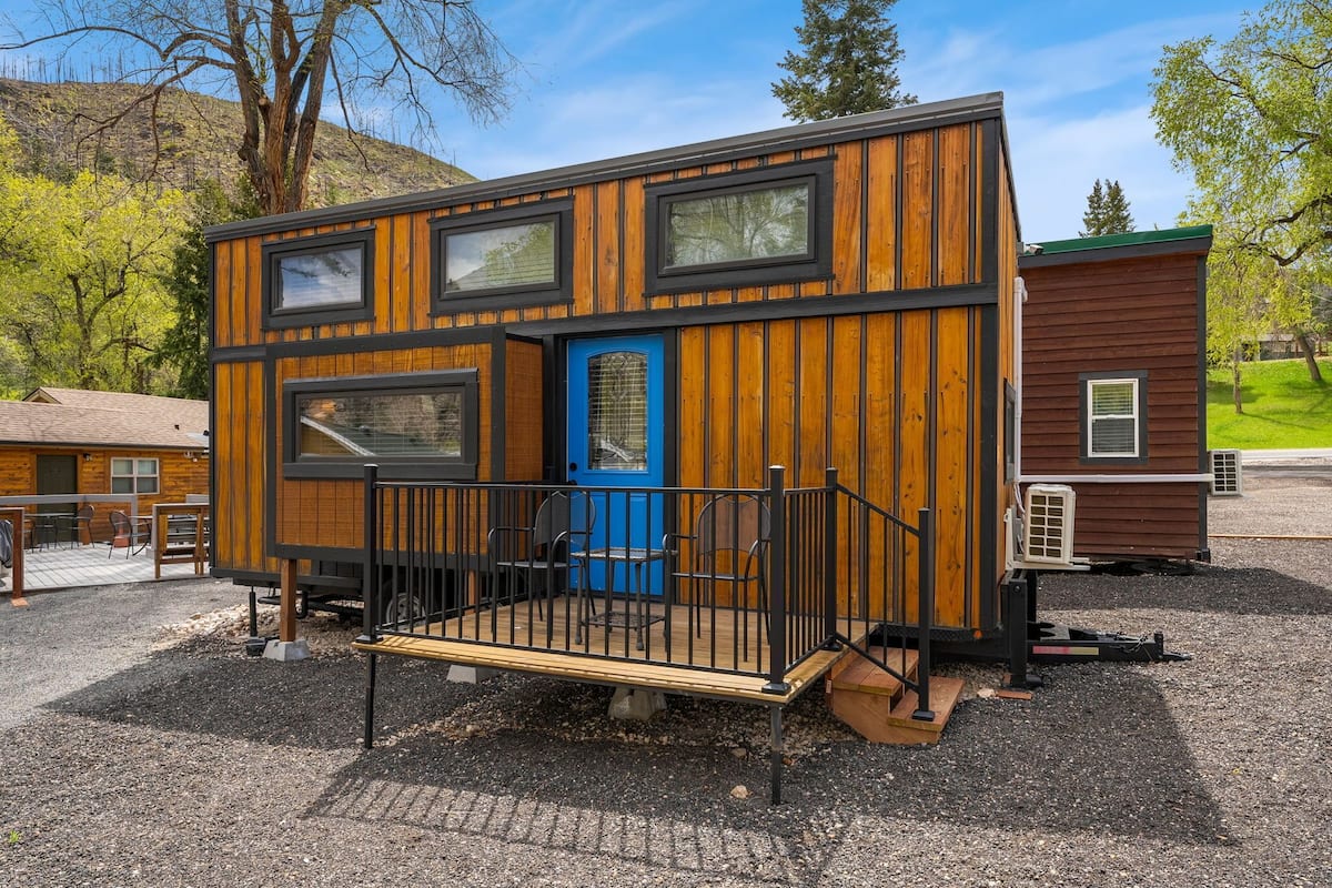 A compact wooden cabin with a blue door, a small deck, and a black railing.