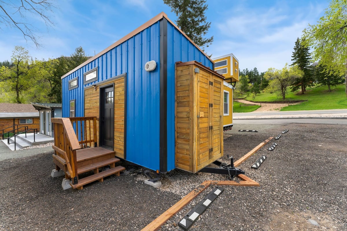 A small, blue and wooden cabin-style building with a wooden staircase and a small porch.