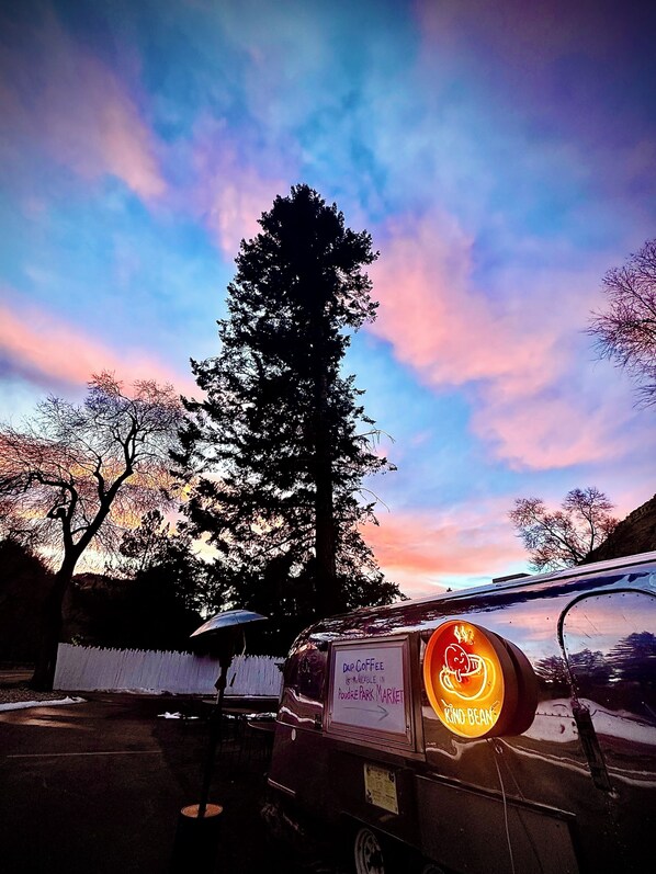 A food truck with a neon sign advertising 'Drip Coffee' and 'Kino Beans' parked in a parking lot with trees and a sunset in the background. - Riverside Colorado (Bellvue)