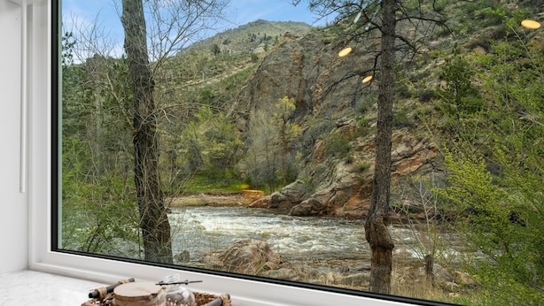 A room with a large window overlooking a rocky river canyon with trees. - Riverside Colorado (Bellvue)